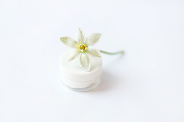 Obraz na płótnie Canvas Ornithogalum flower laying on the top of white cap. Transparent cosmetic jar with white cream. White background. Fresh rain drops. Perfect moisturizer advert.
