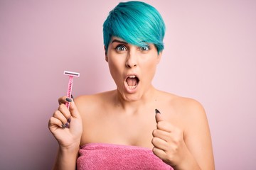 Obraz premium Young woman with blue fashion hair wearing pink towel holding beauty care razor annoyed and frustrated shouting with anger, crazy and yelling with raised hand, anger concept