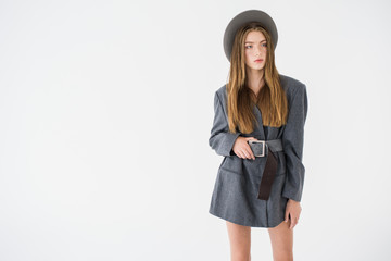 Attractive young girl, model looking to the side in a gray jacket and holding a hat in his hands. Men's style clothing. isolated on a white background. there is a place for an inscription on the side.