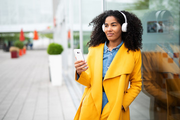 Attraktive junge Frau mit sympathischem Lächeln hält ein Smartphone in der Hand in städtischem Kontext 