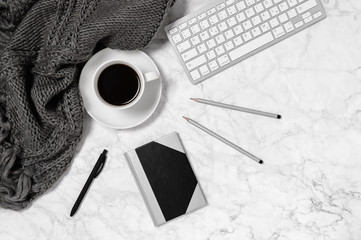 Marble desk with warm wool plaid or scarf, coffee cup, keyboard, notepad, pen and two pencils in black and white