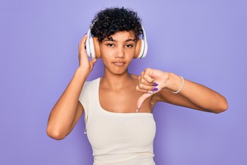 Fototapeta na wymiar Beautiful african american woman listening to music using headphones over red background with angry face, negative sign showing dislike with thumbs down, rejection concept