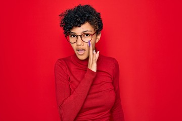 Fototapeta na wymiar Young beautiful african american afro woman wearing turtleneck sweater and glasses hand on mouth telling secret rumor, whispering malicious talk conversation