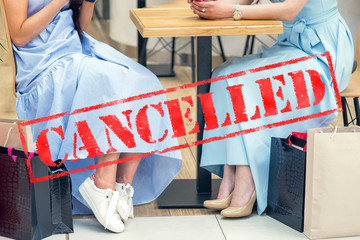 Word CANCELLED on background of two young women in the cafe outdoors. Coronavirus quarantine. Closed cafe outdoors.