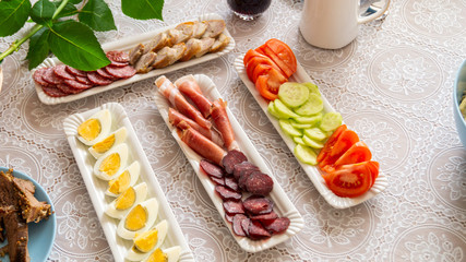 breakfast table: chopped vegetables, sliced meat, boiled eggs on long white porcelain plates on a white tablecloth