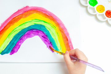 Top view child drawing rainbow with watercolors on the sheet of paper. Children creativity.