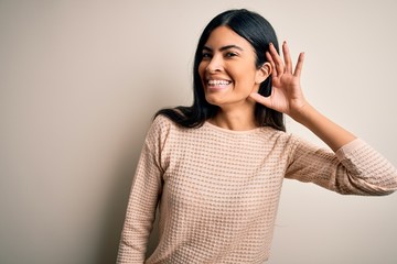 Young beautiful hispanic woman wearing elegant pink sweater over isolated background smiling with hand over ear listening an hearing to rumor or gossip. Deafness concept.