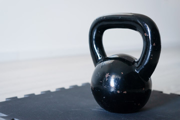 Naklejka na ściany i meble Close up on black iron metal kettlebell griya weight training equipment on the exercise mat on the floor at home in day