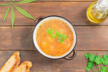 Vegetable cannabis-infused soup in a bowl on wooden table, top view with space for text