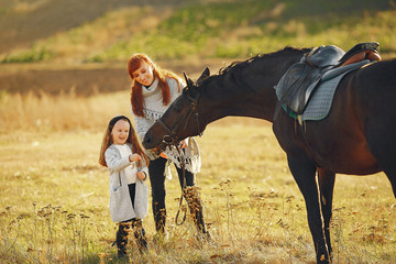 Mother and daughter next to horse. Little girl in a summer field. Family playing with a horse
