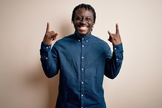 Young handsome african american man wearing casual shirt standing over white background shouting with crazy expression doing rock symbol with hands up. Music star. Heavy music concept.
