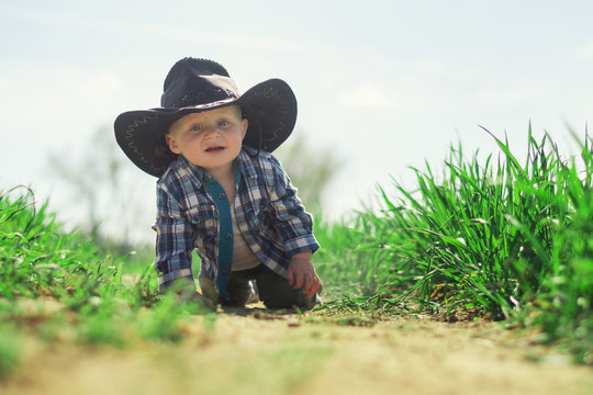A little Caucasian baby boy in a cowboy hat and plaid shirt.