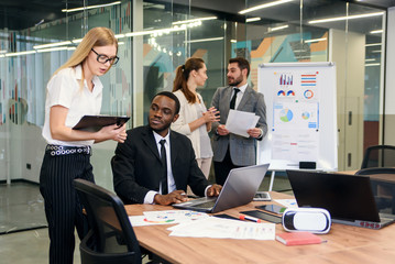 Attractive worker consulting with her office manager and signing financial document at her workplace.