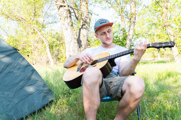 Young man playing guitar outside near camping tent