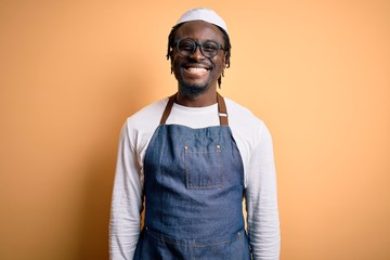 Young african american cooker man wearing apron and over isolated yellow background with a happy...