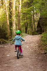 Young girl with green helmet cycling on forest path. Junges Mädchen mit grünem Helm fährt mit Fahrrad auf Waldweg.