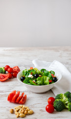 Salad of spinach, avocado, lettuce, tomatoes, broccoli and black olives on a white table.