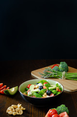 Salad of spinach, avocado, lettuce, tomatoes, broccoli and black olives. Dark photography. 