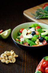 Close up of salad of spinach, avocado, lettuce, tomatoes, broccoli and black olives. Dark photography.