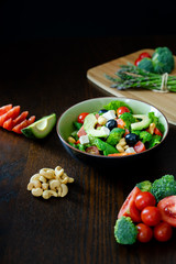 Salad of spinach, avocado, lettuce, tomatoes, broccoli and black olives. Dark photography.