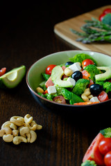 Salad of spinach, avocado, lettuce, tomatoes, broccoli and black olives. Dark photography.