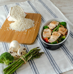 Fuente con salmón salvaje, arroz, esparragos trigueros, brócoli, pimiento rojo y champiñones sobre mesa blanca.
