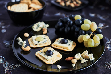 Three blue cheese crackers with grapes are on a black plate.