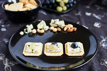 Three blue cheese crackers with grapes are on a black plate.