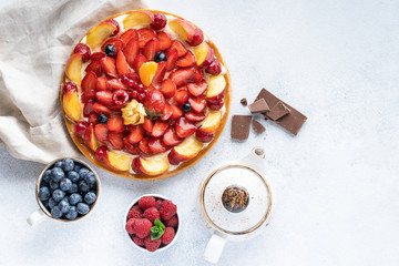 Homemade open tart with strawberries, raspberries, blueberries and grapes on a grey background. Homemade cake. The concept of healthy and delicious food. Top view, copy space.