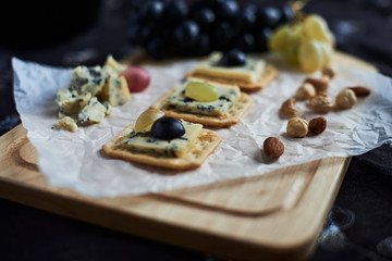Three blue cheese crackers with grapes are on a cutting board.
