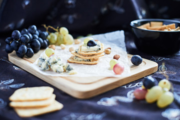 Three blue cheese crackers with grapes are on a cutting board.