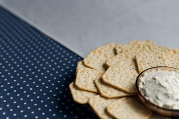 A plate with crackers and curd cheese lying on a polka dot tablecloth.