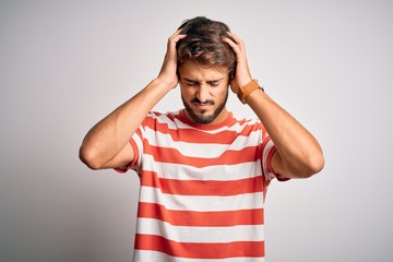 Young handsome man with beard wearing striped t-shirt standing over white background suffering from headache desperate and stressed because pain and migraine. Hands on head.
