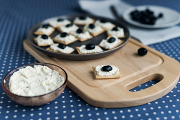 Plate with crackers with soft cheese and olives on a blue polka dot tablecloth.