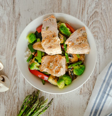 Cenital de bol de salmón salvaje, arroz, esparragos trigueros, brócoli, pimiento rojo, champiñones sobre mesa blanco. 