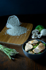 Bol de salmón salvaje, arroz, esparragos trigueros, brócoli, pimiento rojo y champiñones sobre mesa marrón. Dark photography. 