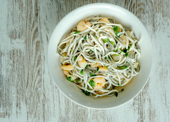 Bol blanco de gulas con gambas, ajos, perejil, guindillas sobre mesa blanca. close up cenital.  