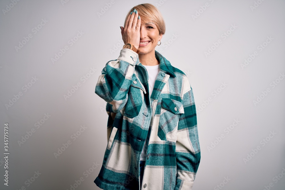 Sticker Young blonde woman with short hair wearing casual retro green shirt over isolated background covering one eye with hand, confident smile on face and surprise emotion.