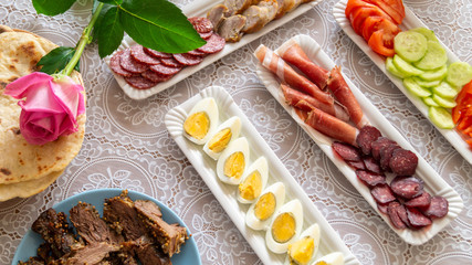 breakfast table: chopped vegetables, sliced meat, boiled eggs on long white porcelain plates on a white tablecloth