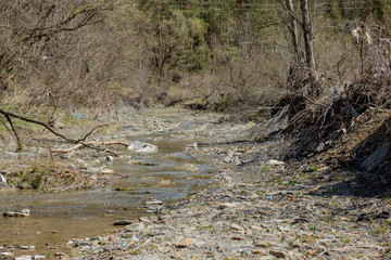 A beautiful small stream is littered with a bunch of garbage, empty bottles, cellophane bags, plastic cans