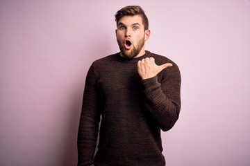 Young blond man with beard and blue eyes wearing casual sweater over pink background Surprised pointing with hand finger to the side, open mouth amazed expression.