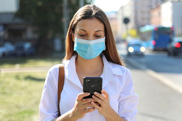 COVID-19 Pandemic Coronavirus Young Woman Wearing Surgical Mask Using Smart Phone App in City...