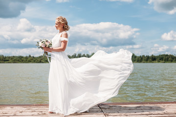 Fototapeta na wymiar beautiful blond girl in long white wedding dress outdoors. Concept of bride going towards future happiness, flying waving skirt