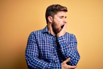 Fototapeta premium Young blond businessman with beard and blue eyes wearing shirt over yellow background bored yawning tired covering mouth with hand. Restless and sleepiness.