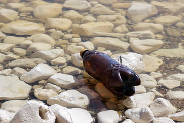 dark plastic bottle on the rocky shore of the river, sea. concept of pollution of rivers, seas and oceans