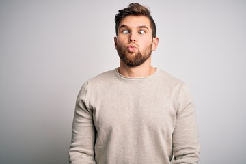 Young handsome blond man with beard and blue eyes wearing casual sweater making fish face with lips, crazy and comical gesture. Funny expression.