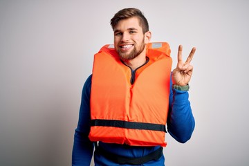 Young blond tourist man with beard and blue eyes wearing lifejacket over white background showing and pointing up with fingers number two while smiling confident and happy.