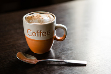 cup of cappuccino and teaspoon on dark wooden table