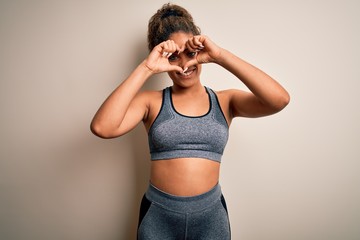 Obraz premium Young african american sportswoman doing sport wearing sportswear over white background Doing heart shape with hand and fingers smiling looking through sign