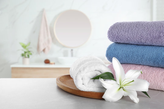 Fresh towels and lily flower on grey table in bathroom. Space for text